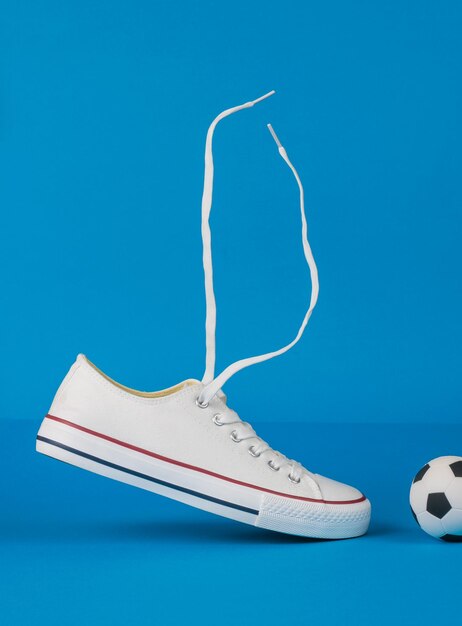 A small soccer ball and a sneaker with rising laces on a blue background