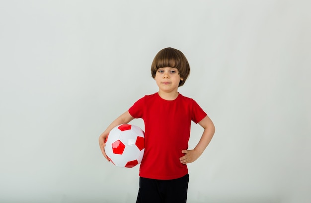 小さなサッカー選手は、テキスト用のスペースがある白い表面にサッカーボールを持っています