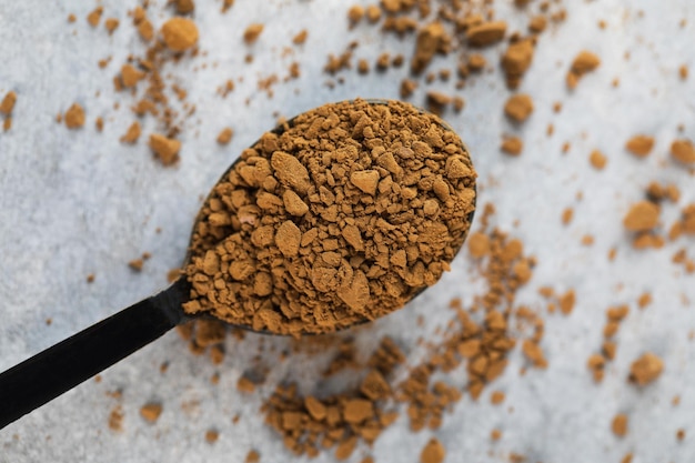 Foto piccolo cucchiaio con granuli di caffè istantaneo sopra un tavolo di pietra grigia in uno studio leggero