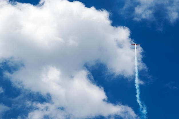 Small sports plane flies straight up into the blue sky with clouds and releasing smoke