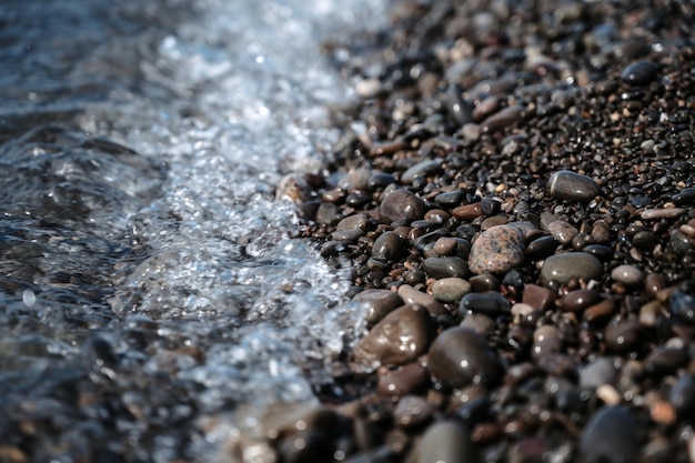 Piccole pietre in primo piano acqua di mare azzurro una foto del mare surf ocean surf tra le rocce sfondo della marea schiuma di mare