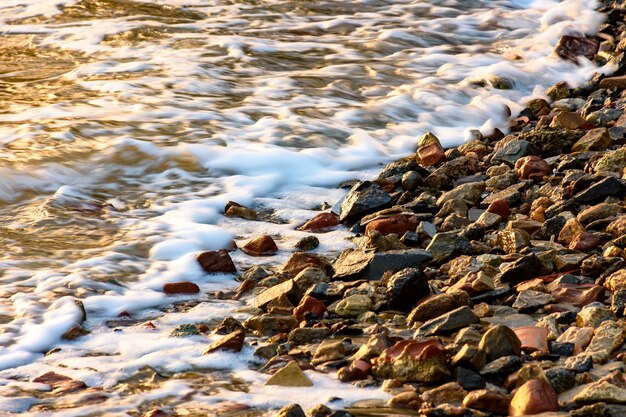 Photo small stones on the shore with the foam of the waves during tropical sunset