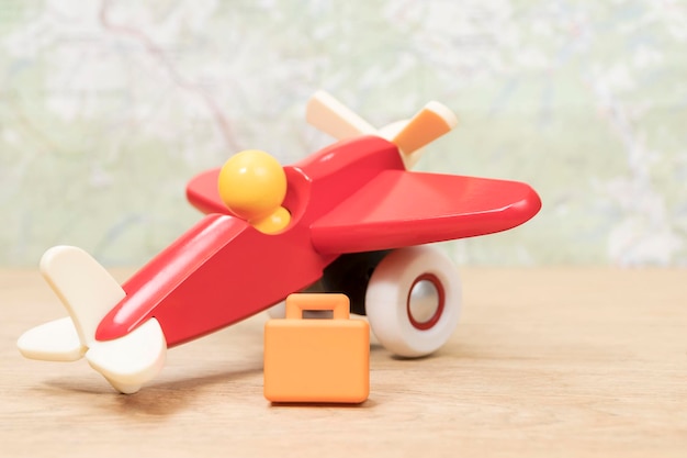 small suitcase and toy plane on the old wooden table on the background of a blurred map