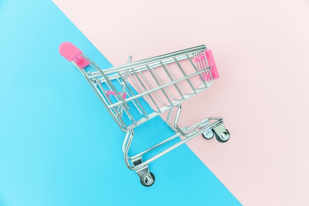 Small supermarket grocery push cart for shopping isolated on blue and pink background