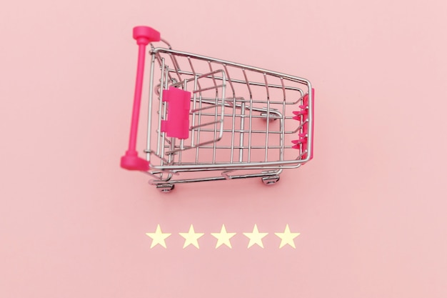 Small supermarket grocery push cart for shopping toy with wheels and 5 stars rating isolated on pastel pink background. Retail consumer buying online assessment and review concept.