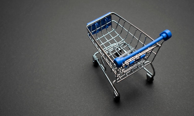 Small supermarket grocery push cart for shopping toy with wheels isolated on dark colourful trendy modern fashion background.