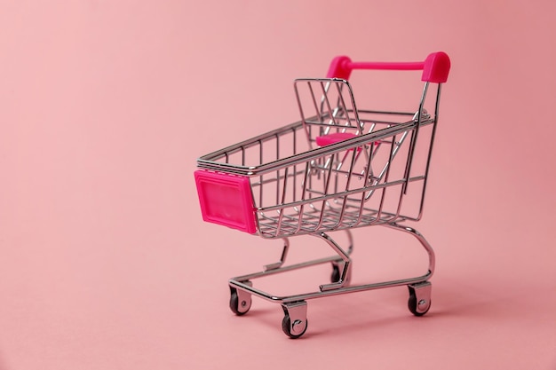 Small supermarket grocery toy push cart on pink background