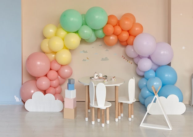 Стол и стулья в интерьере детской комнаты с радугой, разноцветной аркой из воздушных шаров