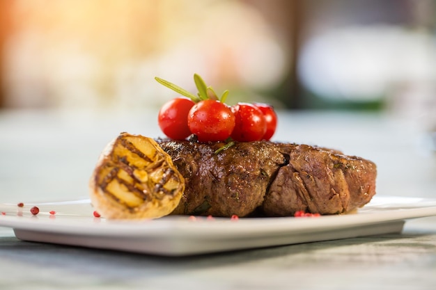 요리된 고기에 작은 토마토. 구운 마늘 조각입니다. 식욕을 돋우는 안심 스테이크. 야채와 함께 제공되는 송아지 고기.