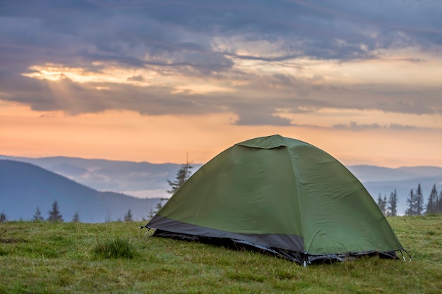 Small tourist tent on grassy mountain hill. Summer camping in mountains at dawn. Tourism concept.