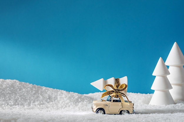 A small toy car transporting Christmas tree in the middle of snowy forest