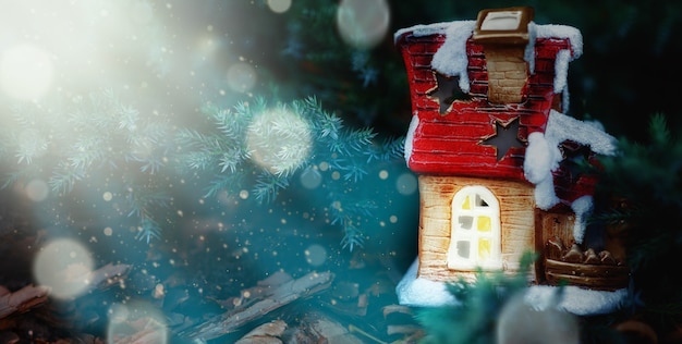 Маленький игрушечный домик со снегом среди новогодних елок и размытыми частицами на заднем плане