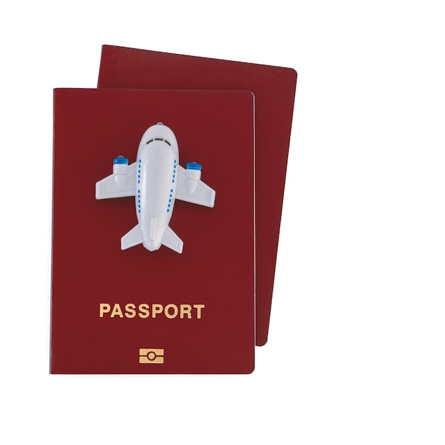 Маленький игрушечный самолет поверх двух красных паспортов на белом фоне