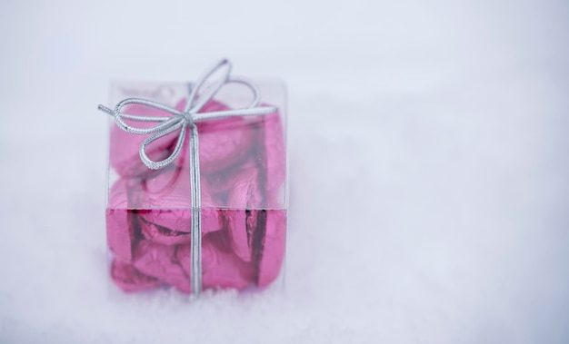 A small transparent box with heartshaped chocolates inside lying on the snow