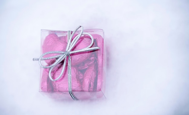 A small transparent box with heartshaped chocolates inside lying on the snow