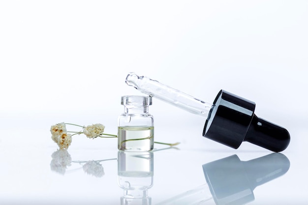 A small transparent glass bottle with an essential oil dropper Aromatherapy and traditional medicine Closeup White background with reflection