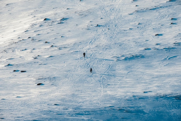 Small two mountaineer hiking on snow covered hill to the top of mountain in winter