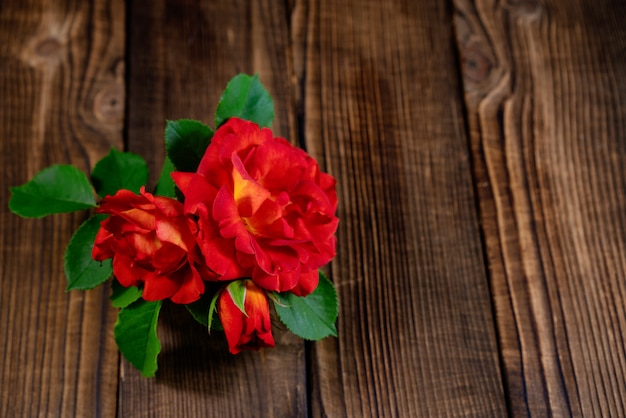 A small vase of red roses on a wooden table.