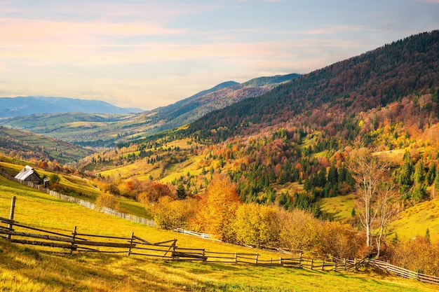 Un piccolo villaggio sotto fantastiche colline ricoperte di foreste colorate autunnali alla luce di un sole caldo e luminoso con il bel tempo