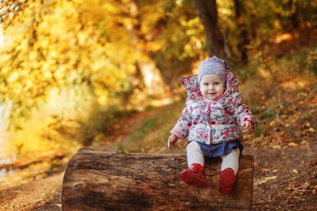 A small warmly dressed girl sits on a log in the Park in autumn