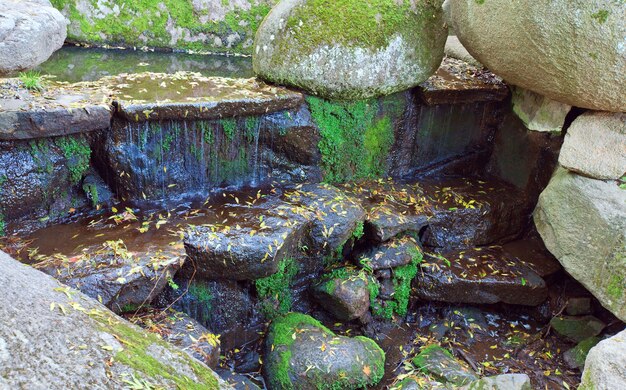 Small waterfall and big boulder in autumn park