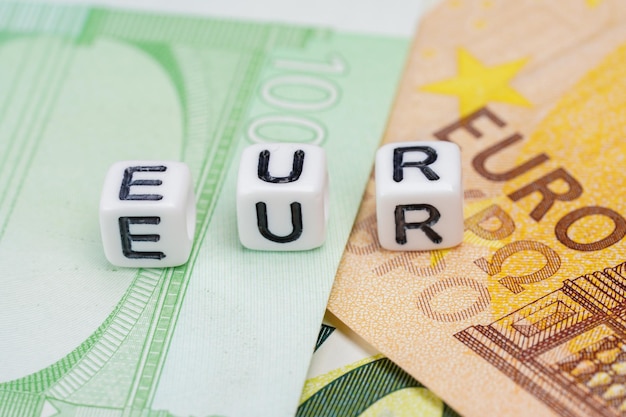 Маленькие белые бусы с буквами EUR на куче евробанкнот вблизи
