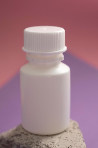 Маленькая белая бутылка с белой крышкой сидит на фиолетово-розовом фоне.