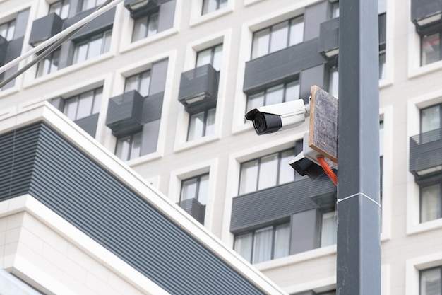 Small white CCTV cameras on a pole against the background of a modern highrise building Security video surveillance face recognition Providing security in a residential area