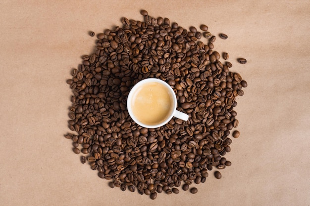 갈색 배경에 볶은 콩에 에스프레소 크레마가 있는 작은 흰색 커피 컵