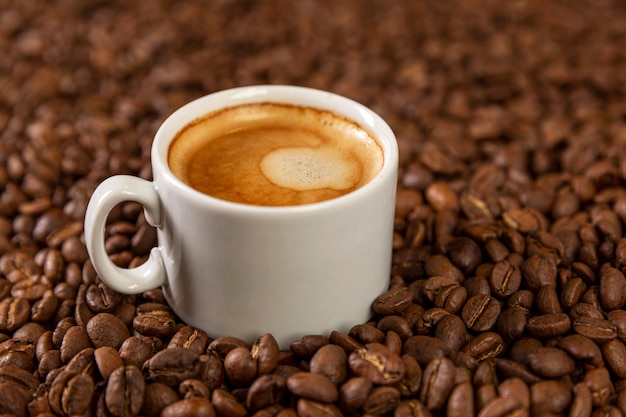 A small white cup of coffee stands on coffee beans. Fragrant pleasure.