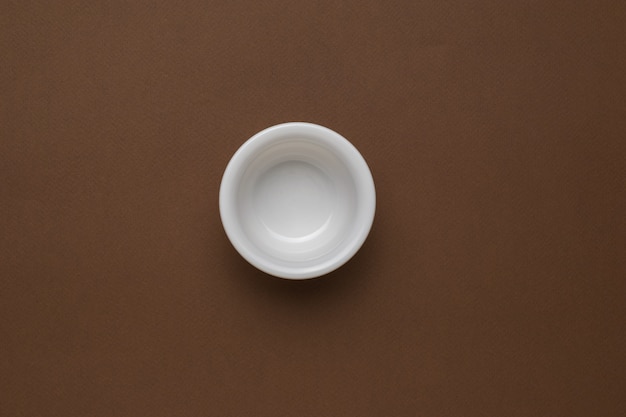 Маленькая белая глубокая чашка на коричневом фоне.