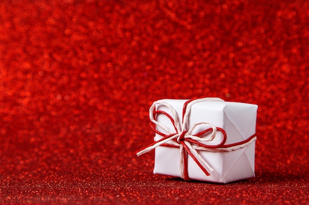 A small white gift on a red shiny, sequins in the side. The concept for Valentine's Day.