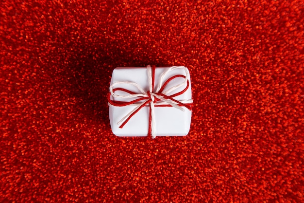 Photo a small white gift on a red shiny, sequins in the side. the concept for valentine's day.