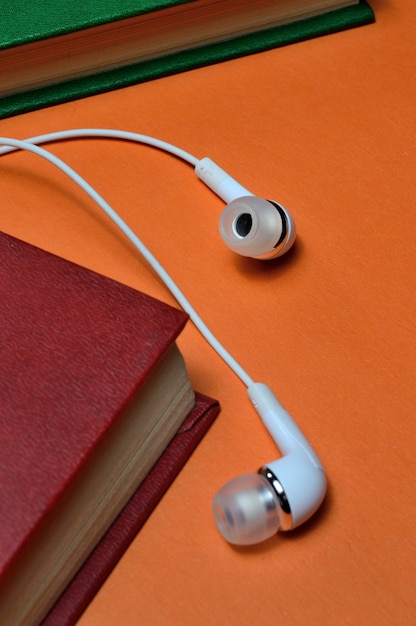 Small white headphones and a stack of books on an orange background.