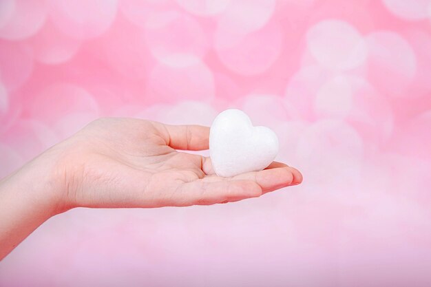 Foto un piccolo cuore bianco in mano su sfondo rosa con bohe. biglietto di auguri di san valentino