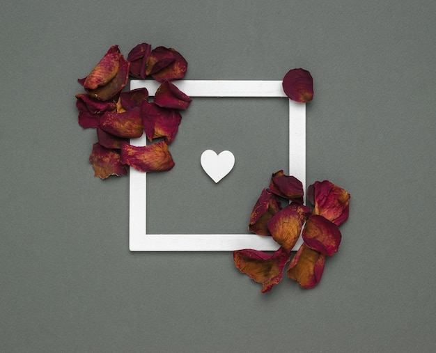 A small white heart inside a white frame with dried rose petals. The form . A place for text and collage.
