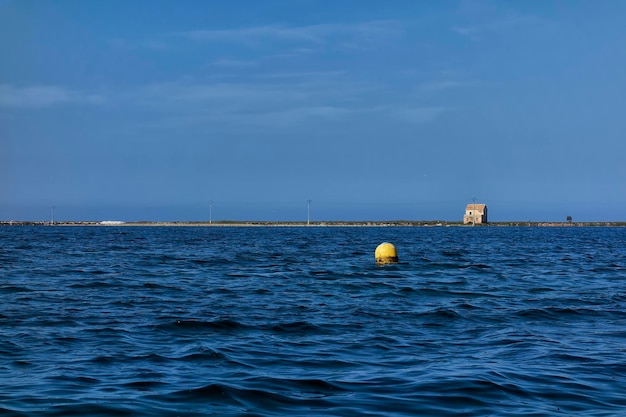 Small white house seen from a boat in the sea on a thin sleeve of land on the Mar Menor in Murcia Spain and a yellow buoy nearby