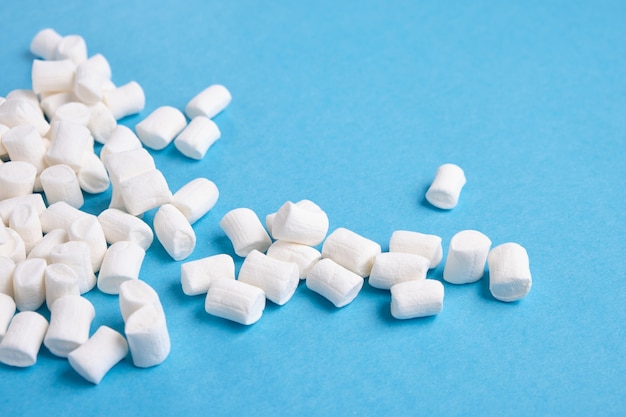 Small white marshmallows scattered on a blue background copy space