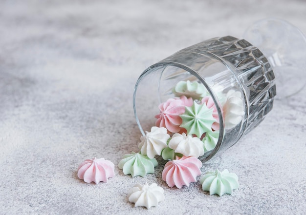 Photo small white pink and green meringues in the glass on concrete background