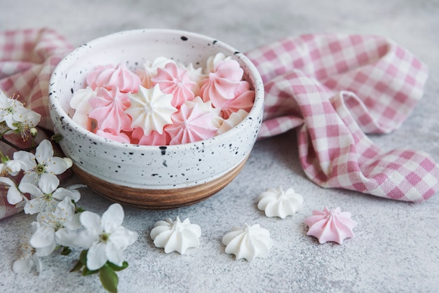 Small white and pink meringues in the ceramic bowl on concrete surface