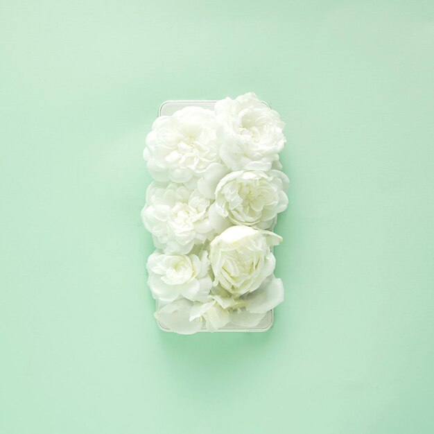 Photo small white roses on a cell phone screen on pastel green backgroundflat lay