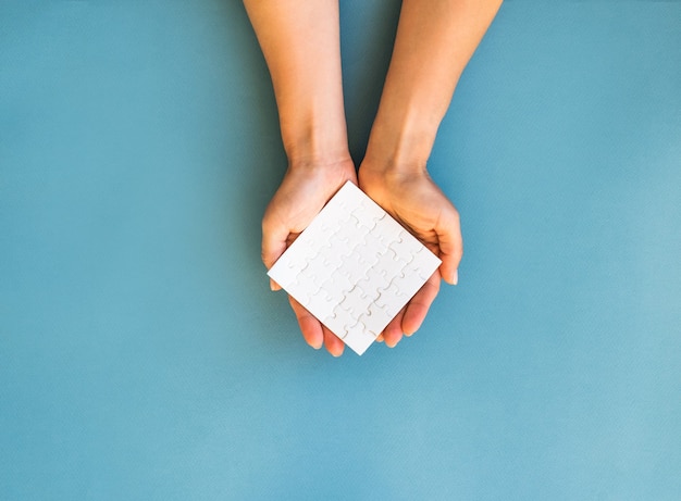 Small white square puzzle in girls hands on a blue