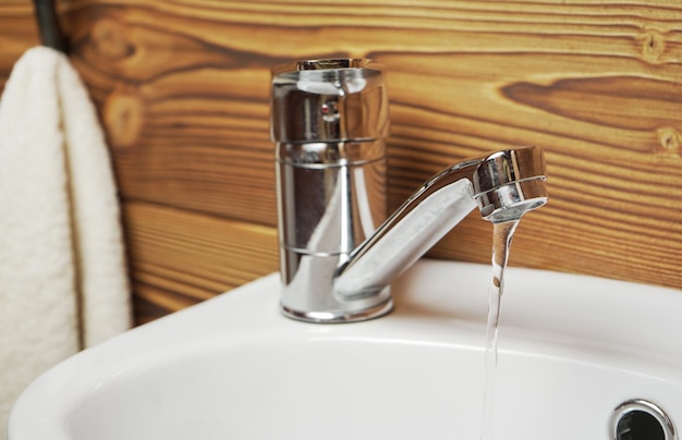 Small white wash basin with water flowing, wooden walls around, closeup detail