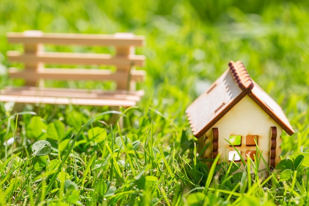 Piccola casa decorativa in legno e piccola panca su erba verde.