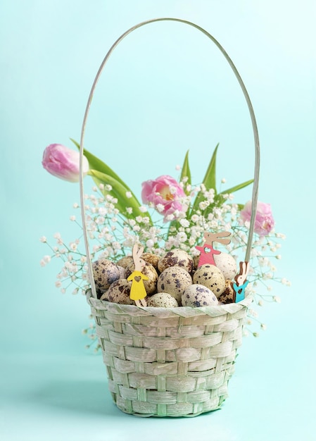 Small wooden Easter bunnies in blue woven basket with quail eggs pink tulips white gypsophila