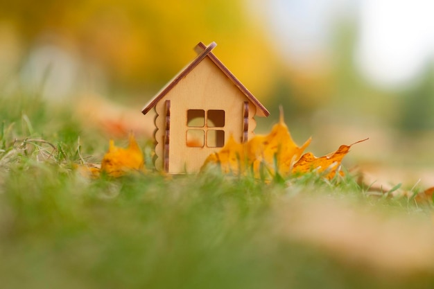 Small wooden house on green grass with autumn leaves Toy house on street in golden autumn Concept of purchasing new apartment and roof overhead