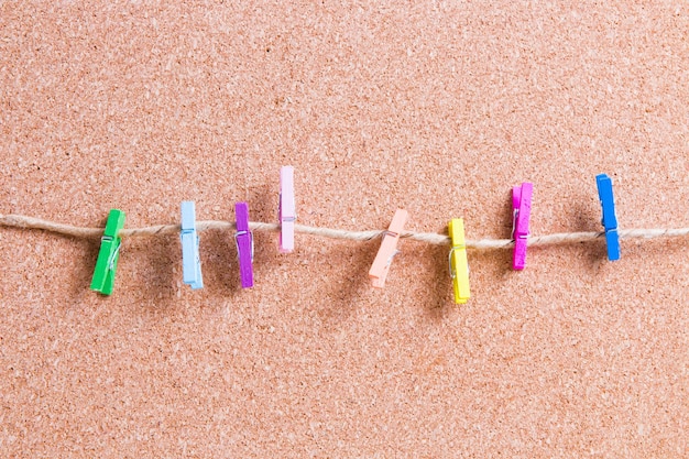 Small wooden paper clothespins on a rope against a corkboard for notes