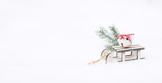 Small wooden sleigh with a New Year's toy on a background of white snow. New year banner