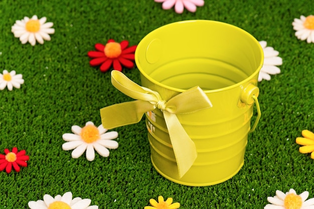 Small yellow empty bucket on artificial green grass with flowers