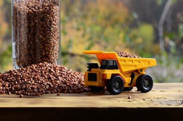 A small yellow toy truck is loaded with brown grains of buckwheat 